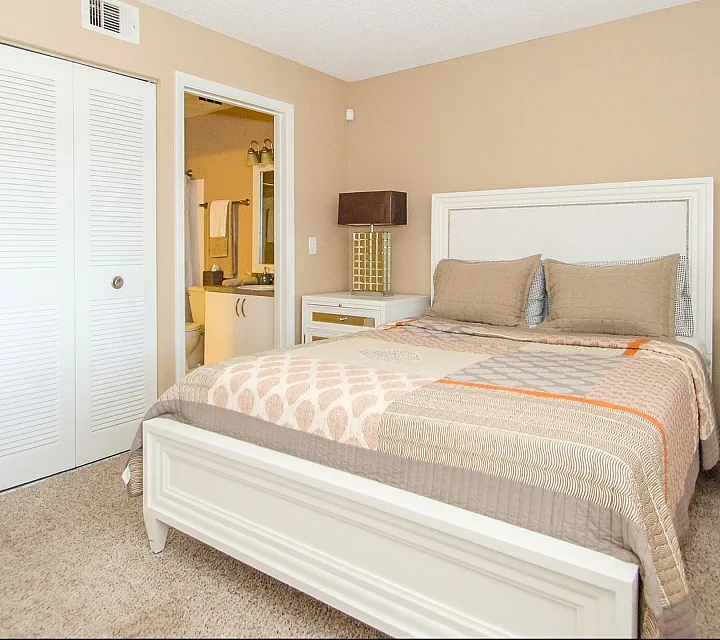 Inviting bedroom with elegant beige walls, cozy bed, matching bedside tables, and soft carpeting, featuring an en-suite bathroom for added convenience.