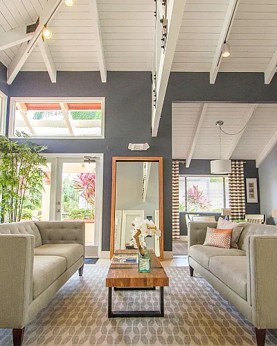 Bright, open living room with high ceilings, elegant cream sofas, and abundant natural light from large windows overlooking greenery.