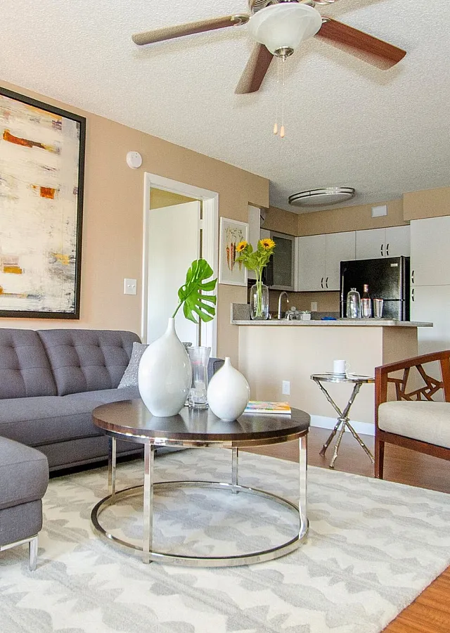 Modern open-concept living space featuring a chic gray sofa, abstract artwork, elegant dining area, and stylish kitchen with sleek cabinets.