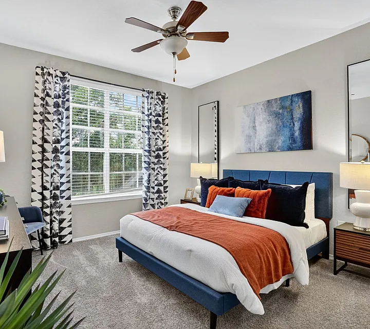 Elegant bedroom with cozy blue bed, vibrant orange accents, and large window with scenic view.