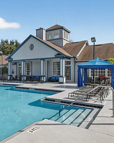 Charming clubhouse with a sparkling pool, sun loungers, gazebo, and lush landscaping, perfect for relaxation and gatherings.