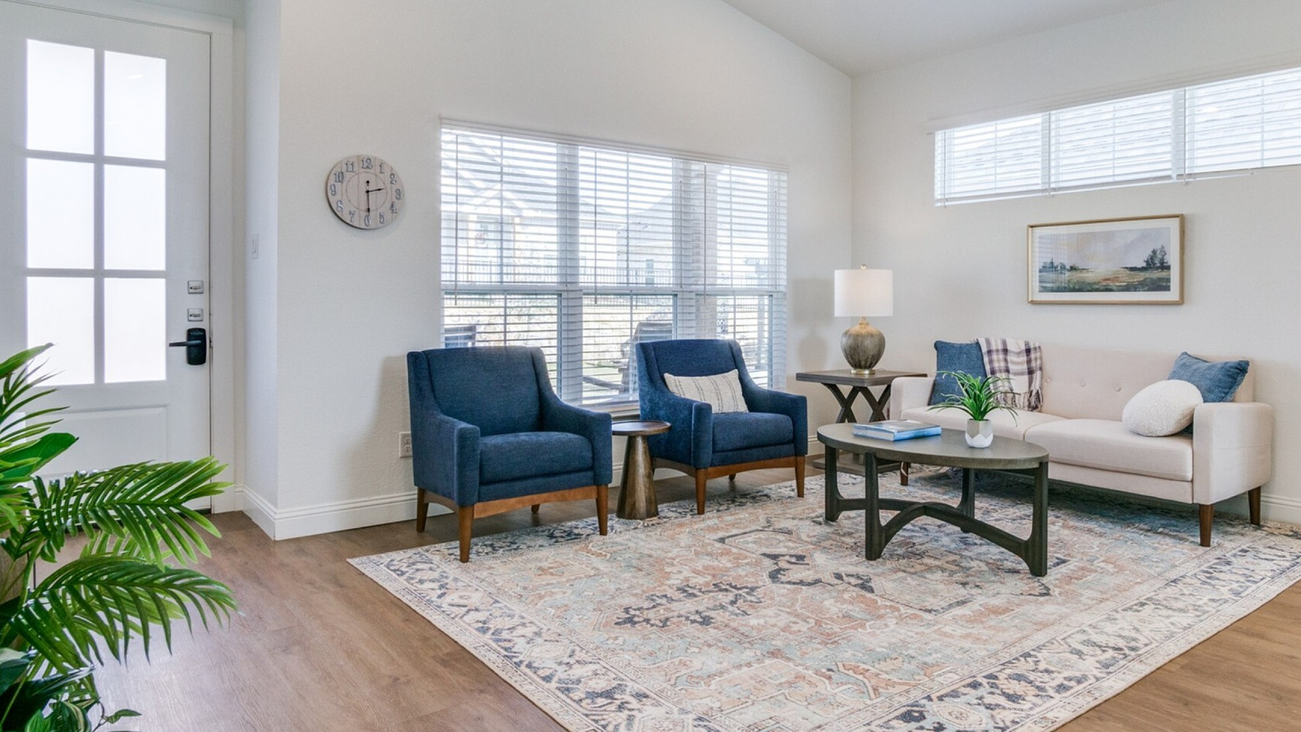 Bright and inviting living room featuring elegant blue armchairs, a chic area rug, and large windows offering natural light.