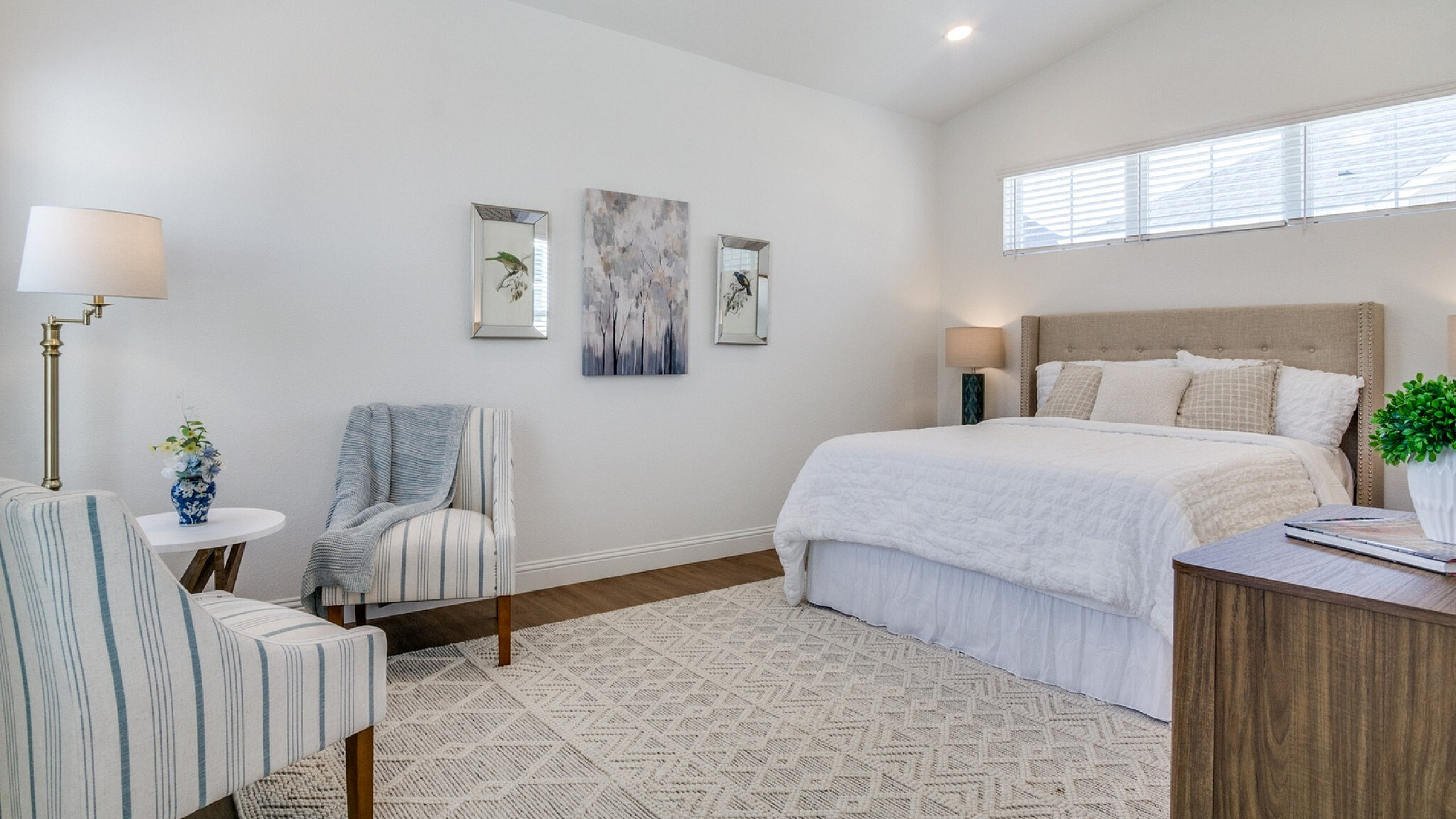 Elegant bedroom with plush bedding, striped upholstered chairs, and stylish decor accents, perfect for relaxation.