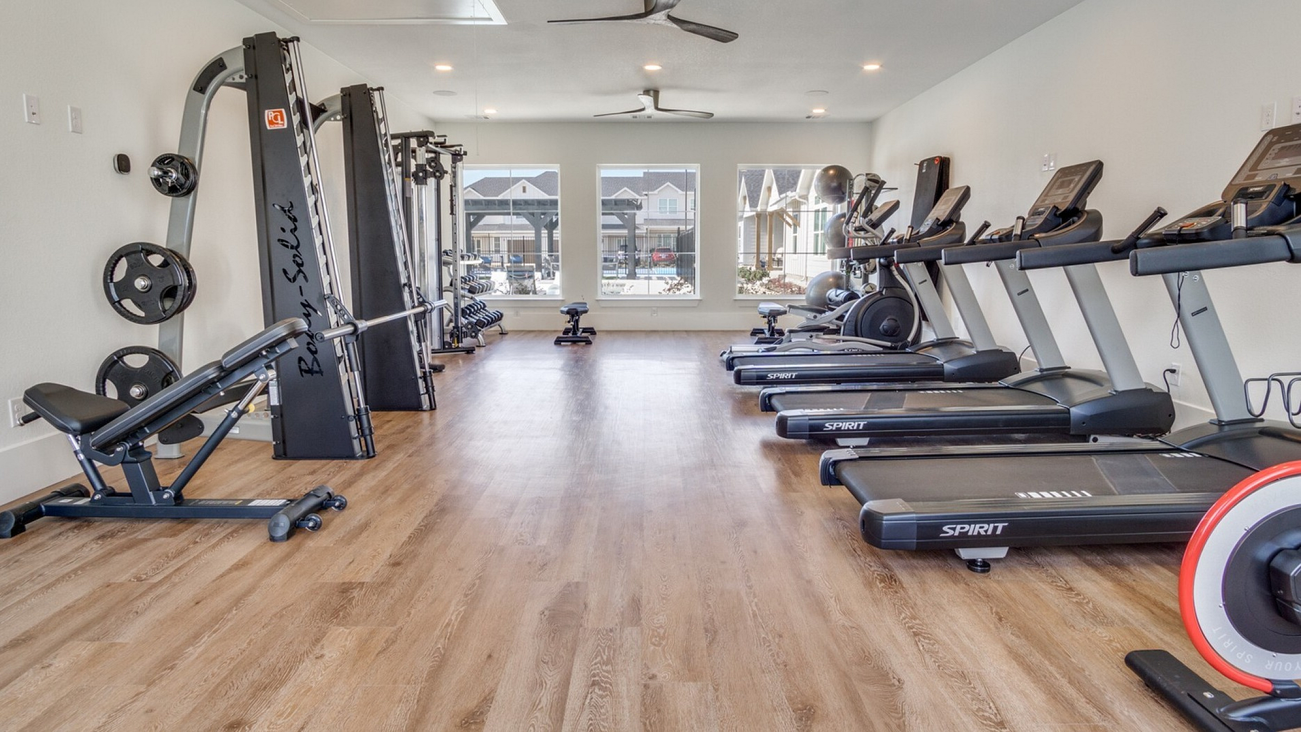 Spacious, modern fitness center with state-of-the-art equipment and natural light from large windows, perfect for an invigorating workout.