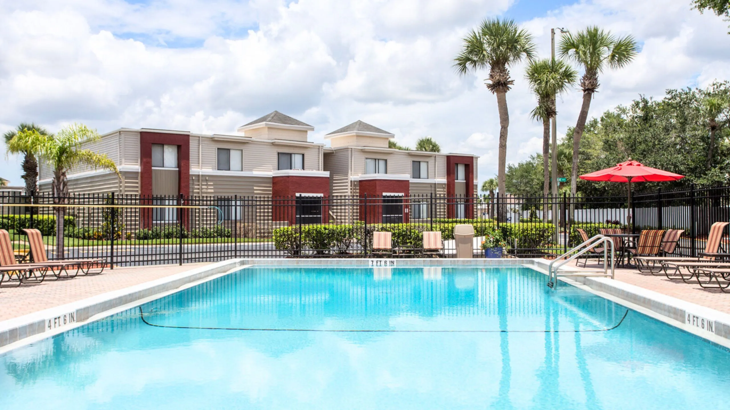 Inviting apartment complex with a sparkling swimming pool, surrounded by lush palm trees and modern, stylish buildings.