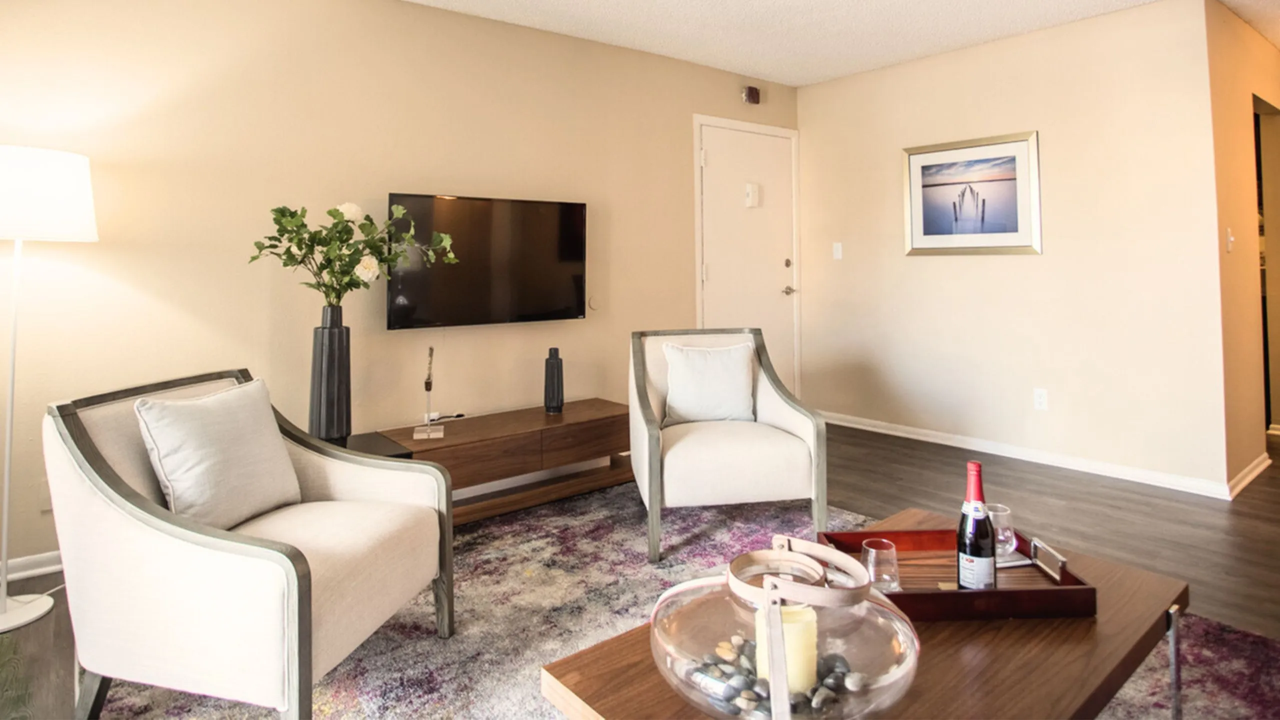 Elegant living room with contemporary decor, featuring cozy armchairs, a stylish wooden coffee table, and a large wall-mounted TV, accented by a vibrant area rug and tasteful artwork.