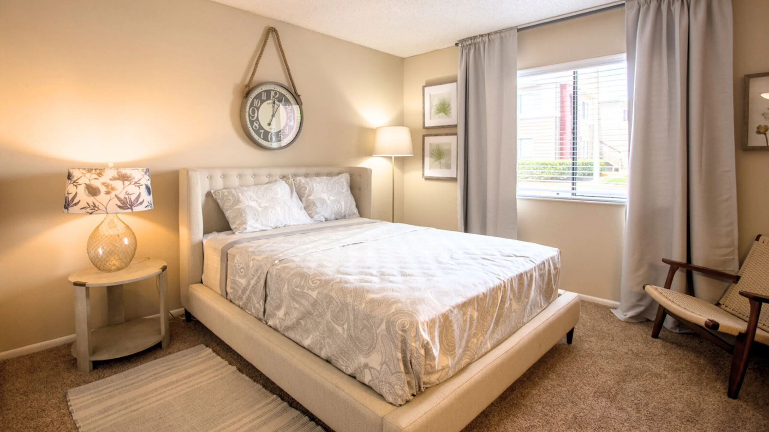 Inviting bedroom with a plush upholstered bed, elegant lamp, and large window flooding the room with natural light.