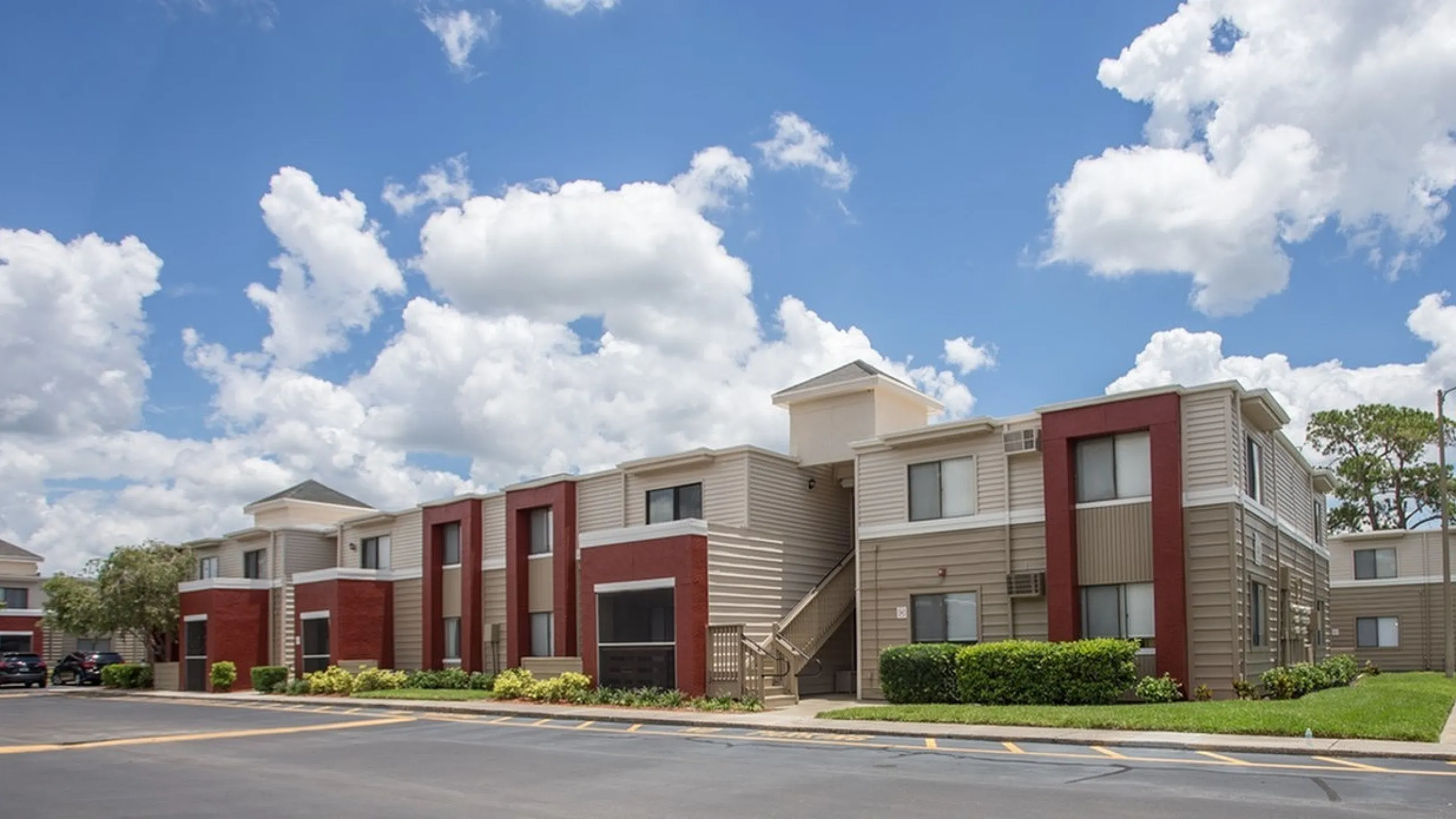 Modern apartment complex with vibrant red and beige exteriors under a bright blue sky, offering stylish living spaces in a peaceful neighborhood.