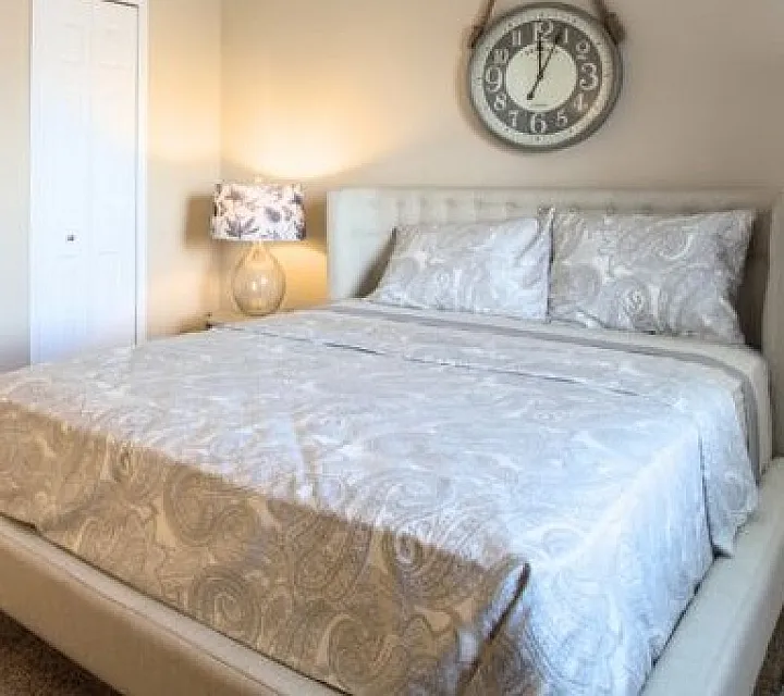 Elegant bedroom featuring a plush king-sized bed with luxurious bedding, chic decor, and a vintage wall clock.
