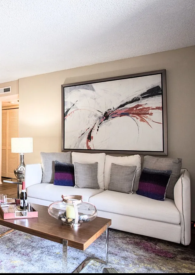 Elegant living room with modern artwork, chic white sofa, and stylish dining area, creating a cozy and inviting atmosphere.