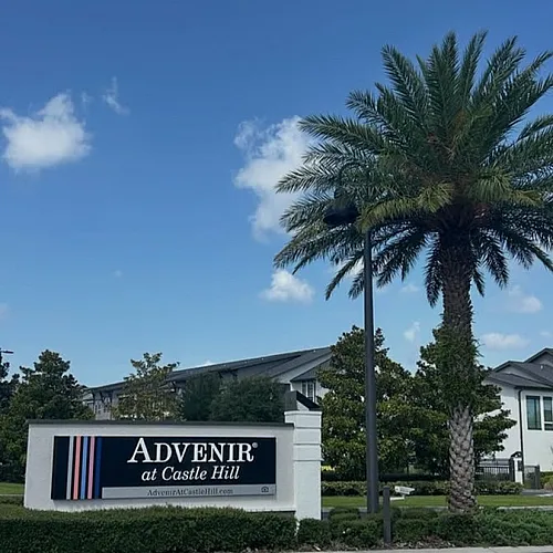 Inviting entrance at Advenir at Castle Hill with lush palm trees and modern architecture under a clear blue sky.