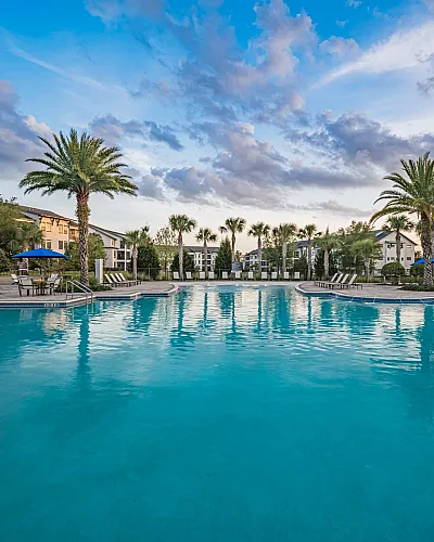 Luxurious apartment community with a stunning, palm-lined resort-style pool under a picturesque sky.