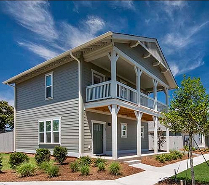Charming two-story home with a spacious balcony, surrounded by lush greenery and stunning blue skies, perfect for modern living.
