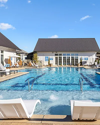 Inviting outdoor pool area with sleek lounge chairs and a modern clubhouse, set against a clear blue sky.