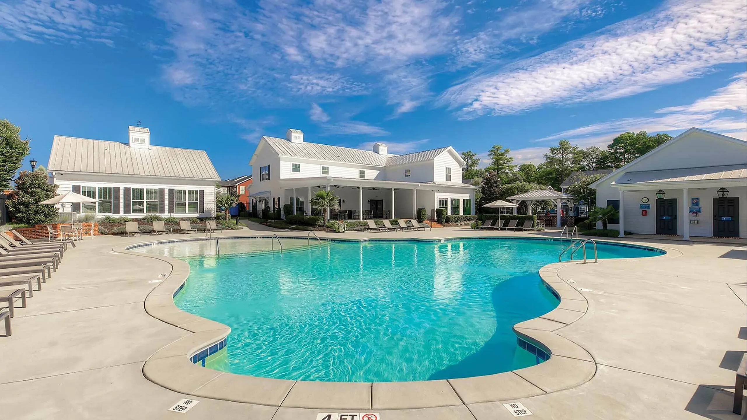 Inviting resort-style swimming pool with elegant poolside seating and charming white cottages under a vibrant blue sky.
