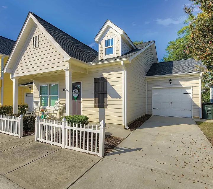 Charming suburban home with inviting front porch, white picket fence, and vibrant yellow siding, perfect for serene living.