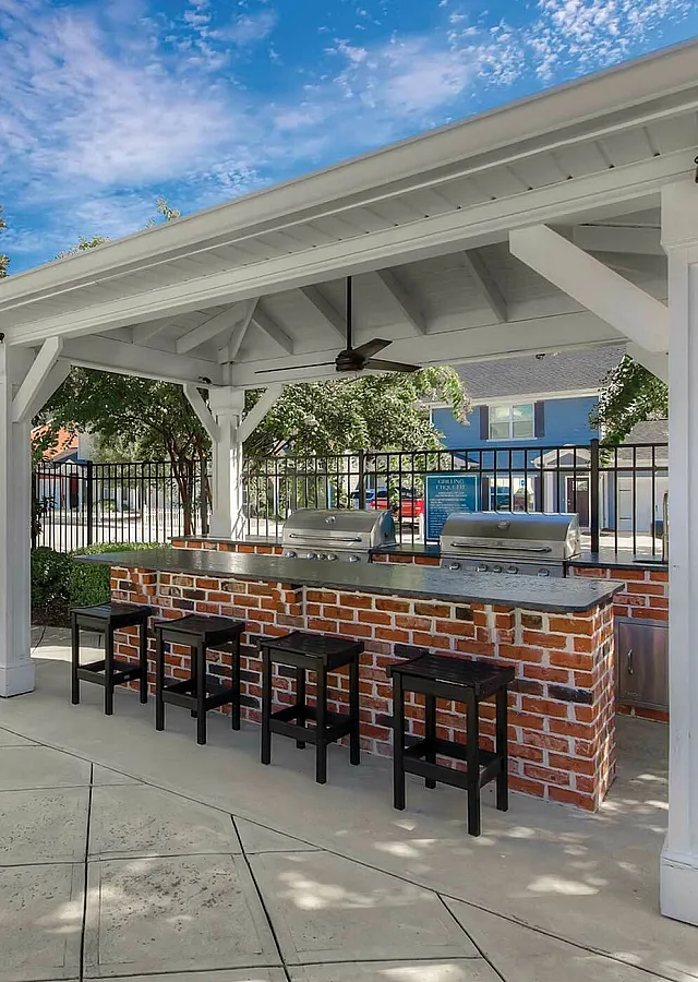 Charming outdoor kitchen with brick bar, three bar stools, and a modern grill under a stylish pergola, ideal for entertaining.