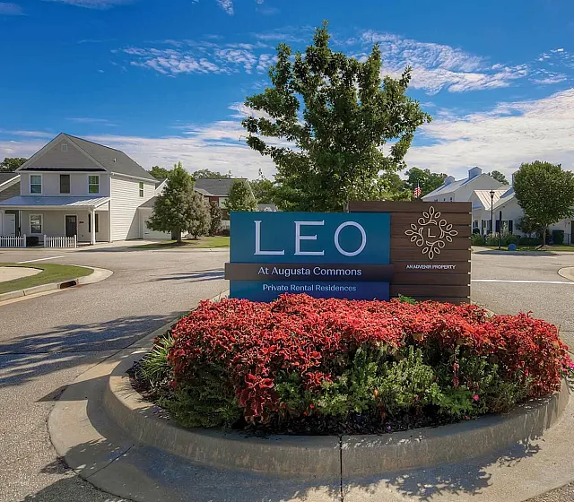 Charming community entrance at LEO Augusta Commons, surrounded by lush landscaping and modern homes under a clear blue sky.