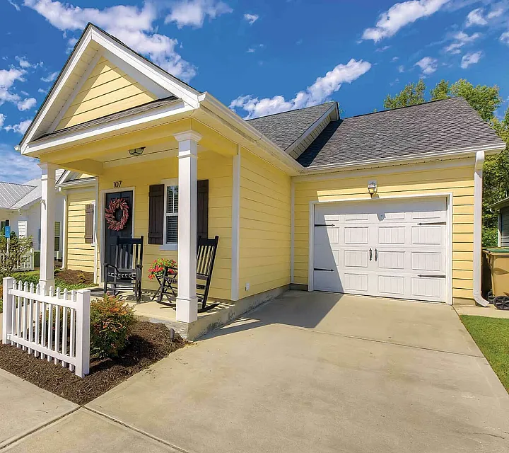 Charming yellow cottage with inviting front porch and white picket fence under a bright blue sky.
