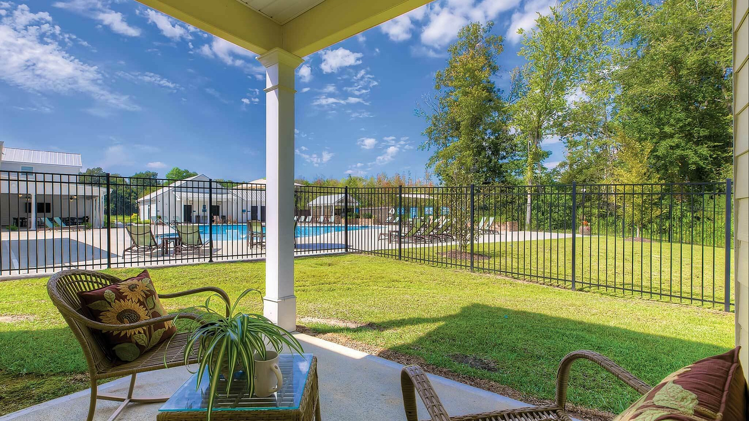 Charming patio with wicker furniture overlooks a refreshing swimming pool and vibrant green lawn, creating a serene outdoor retreat.