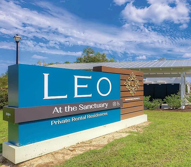 Inviting entrance to LEO at the Sanctuary with vibrant signage and well-maintained greenery, under a clear blue sky.