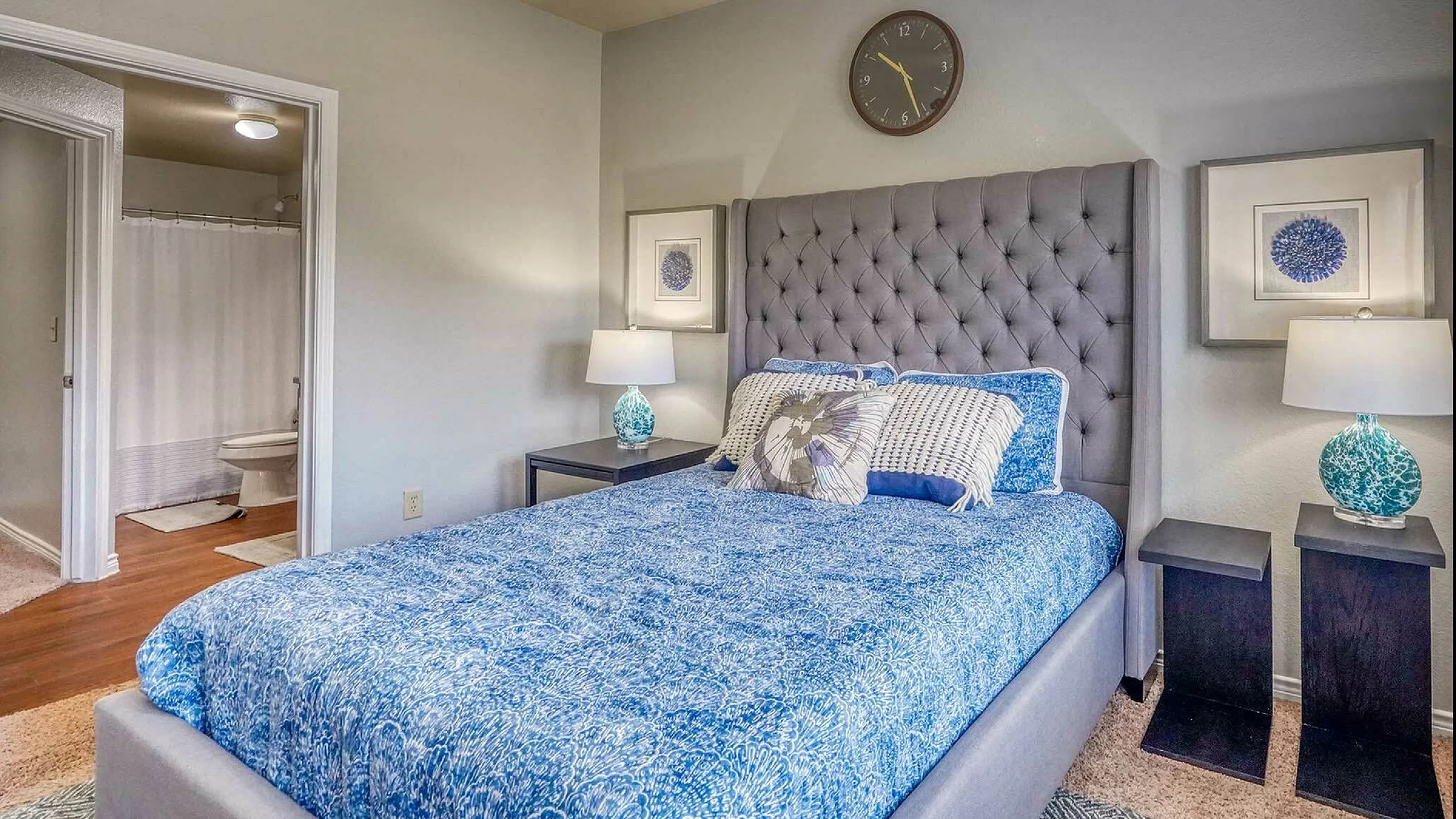 Inviting bedroom with elegant decor, featuring a plush upholstered bed, vibrant blue bedding, and stylish bedside lamps, highlighting a seamless access to an en-suite bathroom.