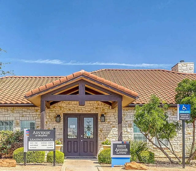 Charming apartment leasing office with rustic stone exterior and inviting red-tiled roof under a clear blue sky.
