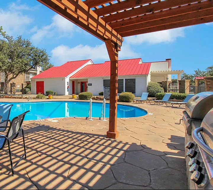 Inviting outdoor pool area with stylish loungers, vibrant red-roofed clubhouse, and shaded seating, perfect for relaxation and entertainment.