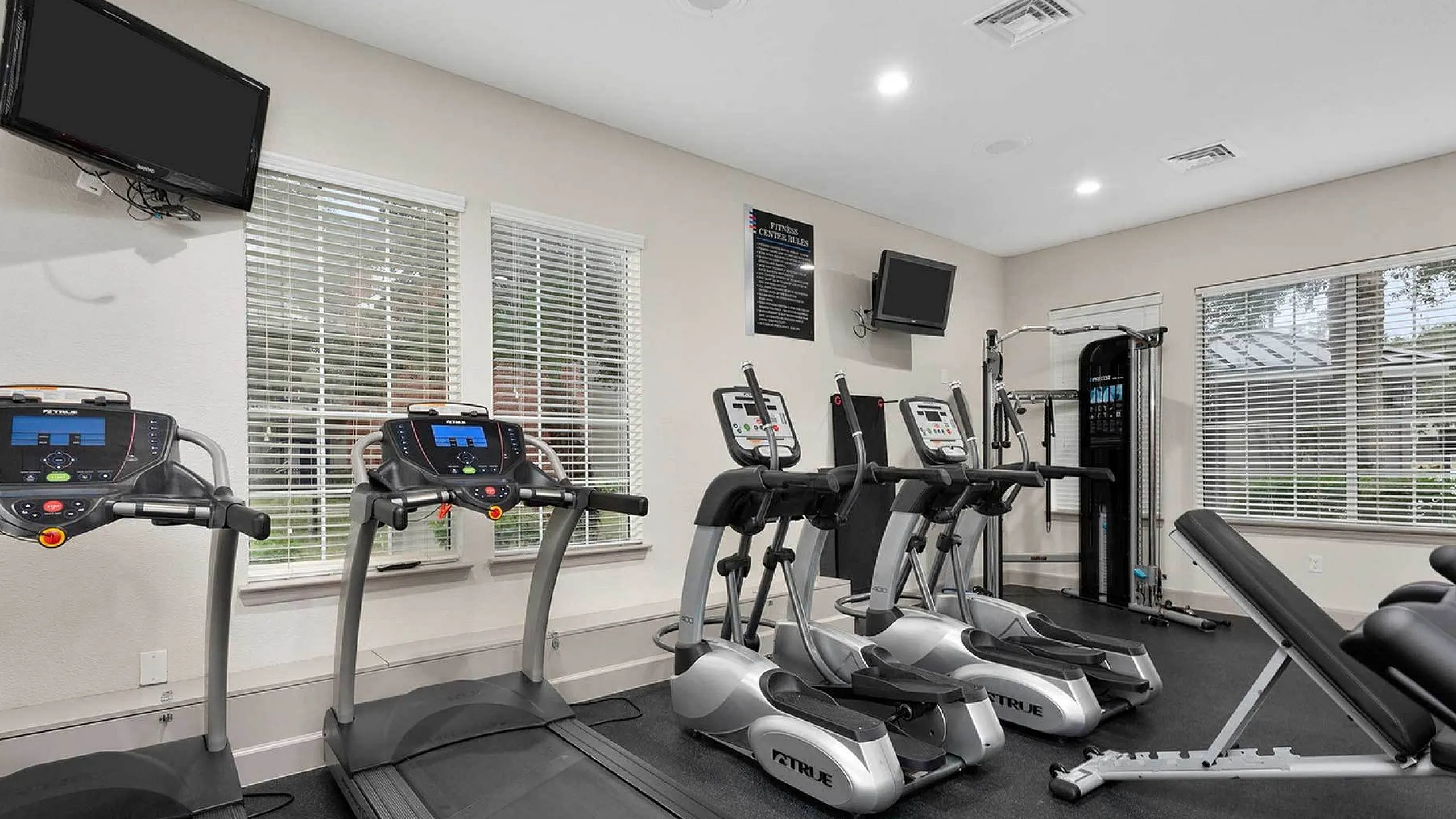 Modern fitness center with state-of-the-art treadmills, ellipticals, and weight bench in a bright, spacious room.