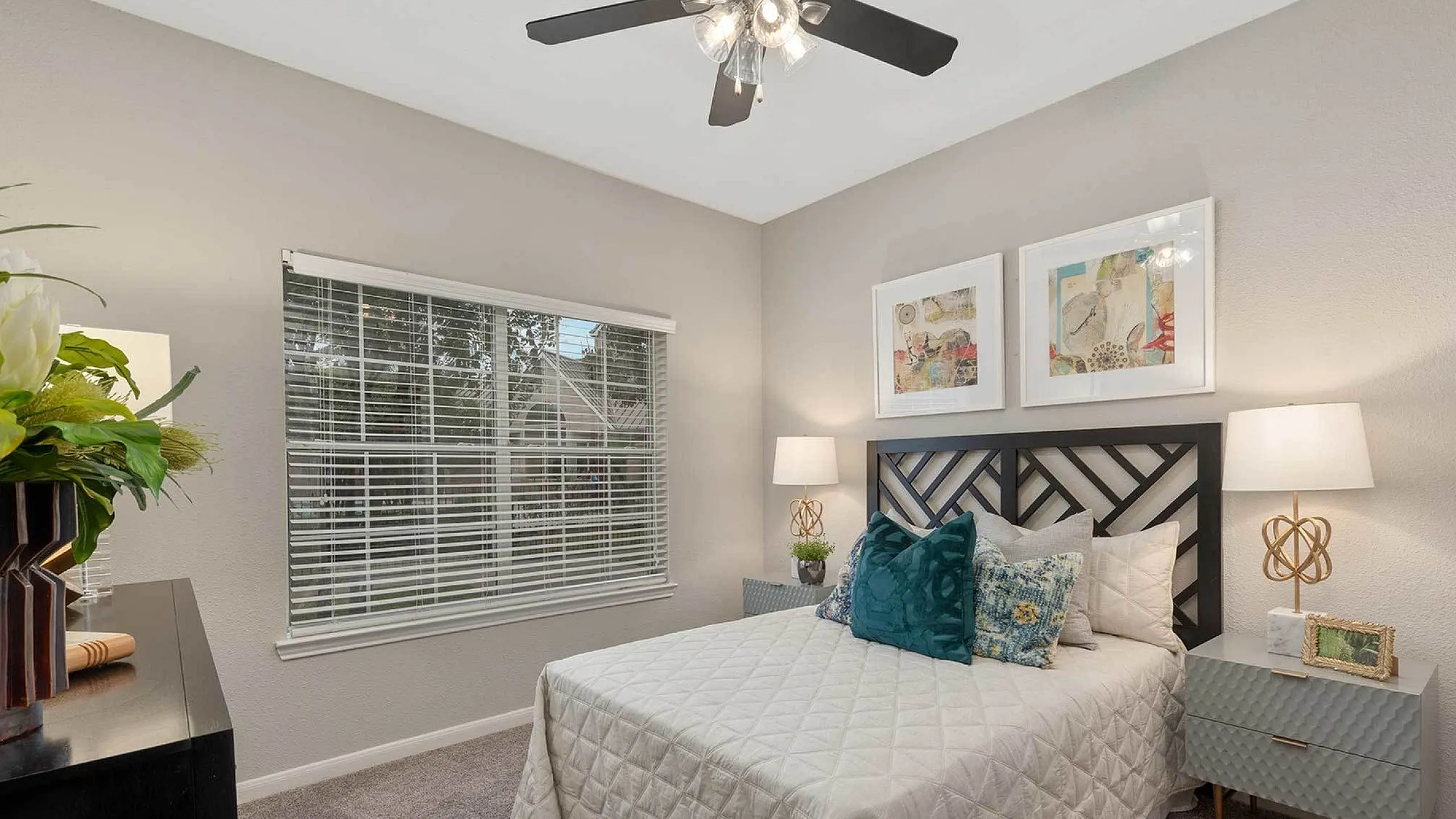 Cozy bedroom with elegant decor, featuring a plush bed with decorative pillows, stylish nightstands, and modern wall art under a sleek ceiling fan.