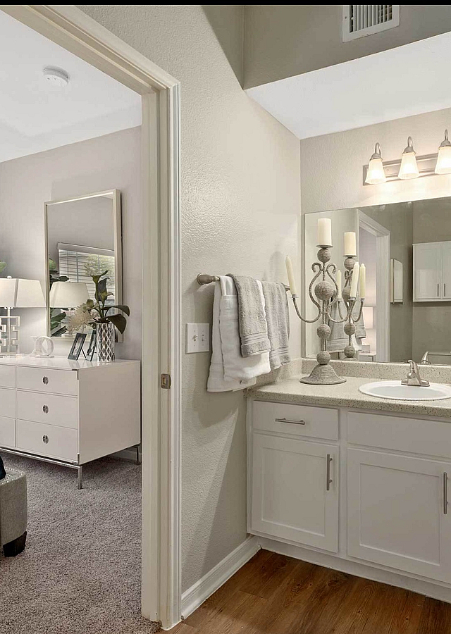 Elegant apartment interior showcasing a bright bathroom with dual sinks and a modern bedroom featuring plush decor and stylish lighting.