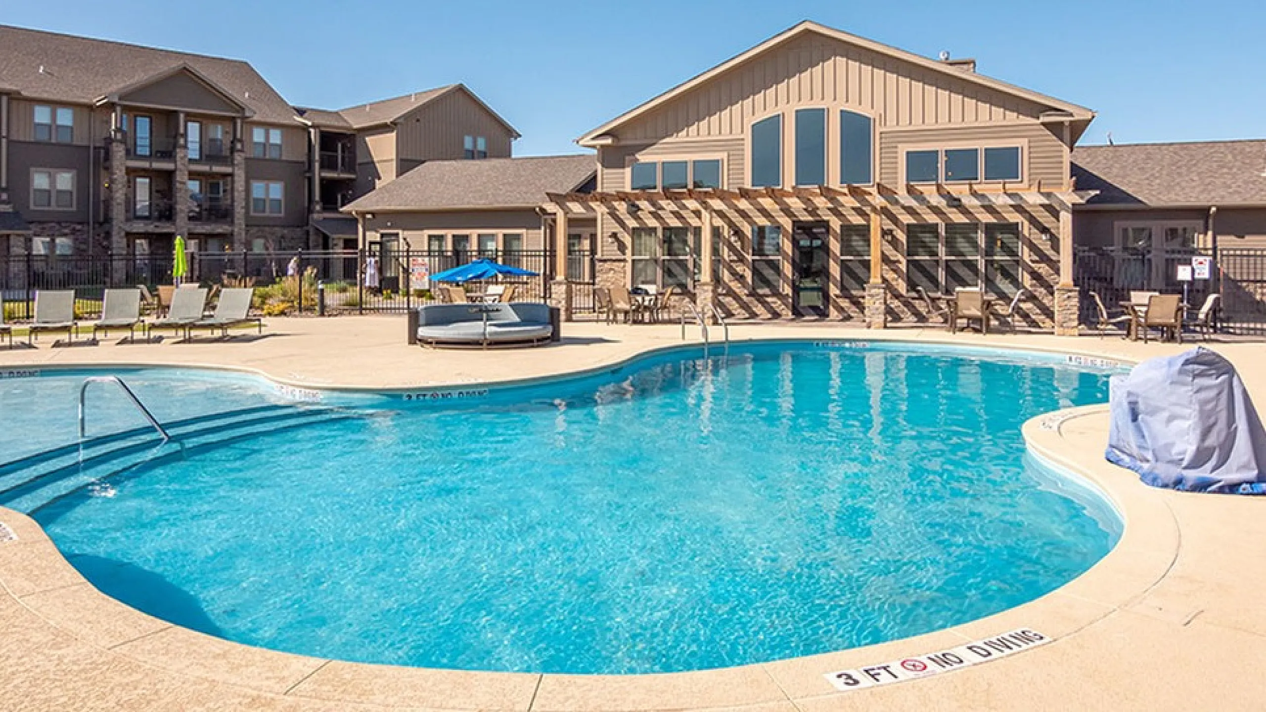Inviting outdoor pool area with sun loungers and modern apartment complex in the background, perfect for relaxation and leisure.