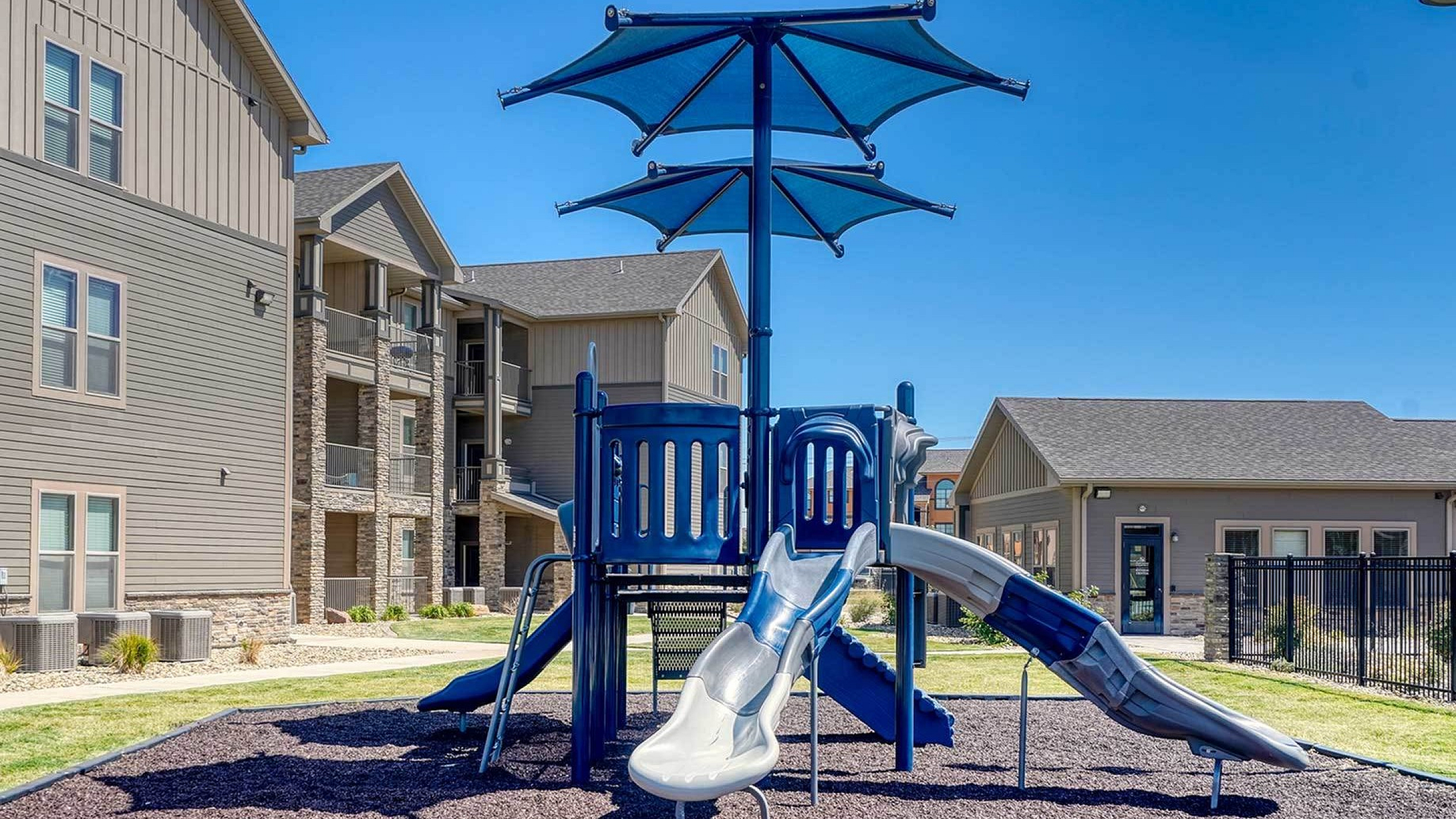 Charming apartment complex featuring a modern playground with slides and shade, ideal for family-friendly living.