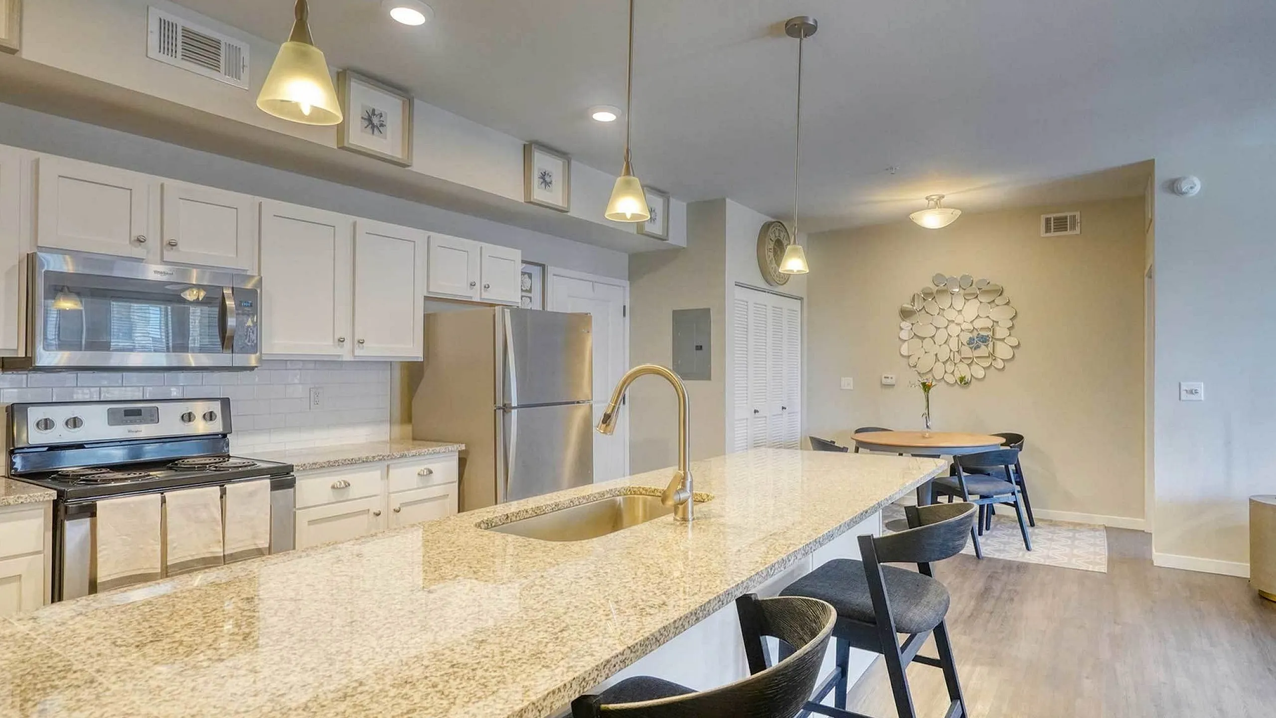 Modern apartment kitchen featuring sleek granite countertops, stainless steel appliances, and stylish pendant lighting, with an open view of the dining area and contemporary decor.