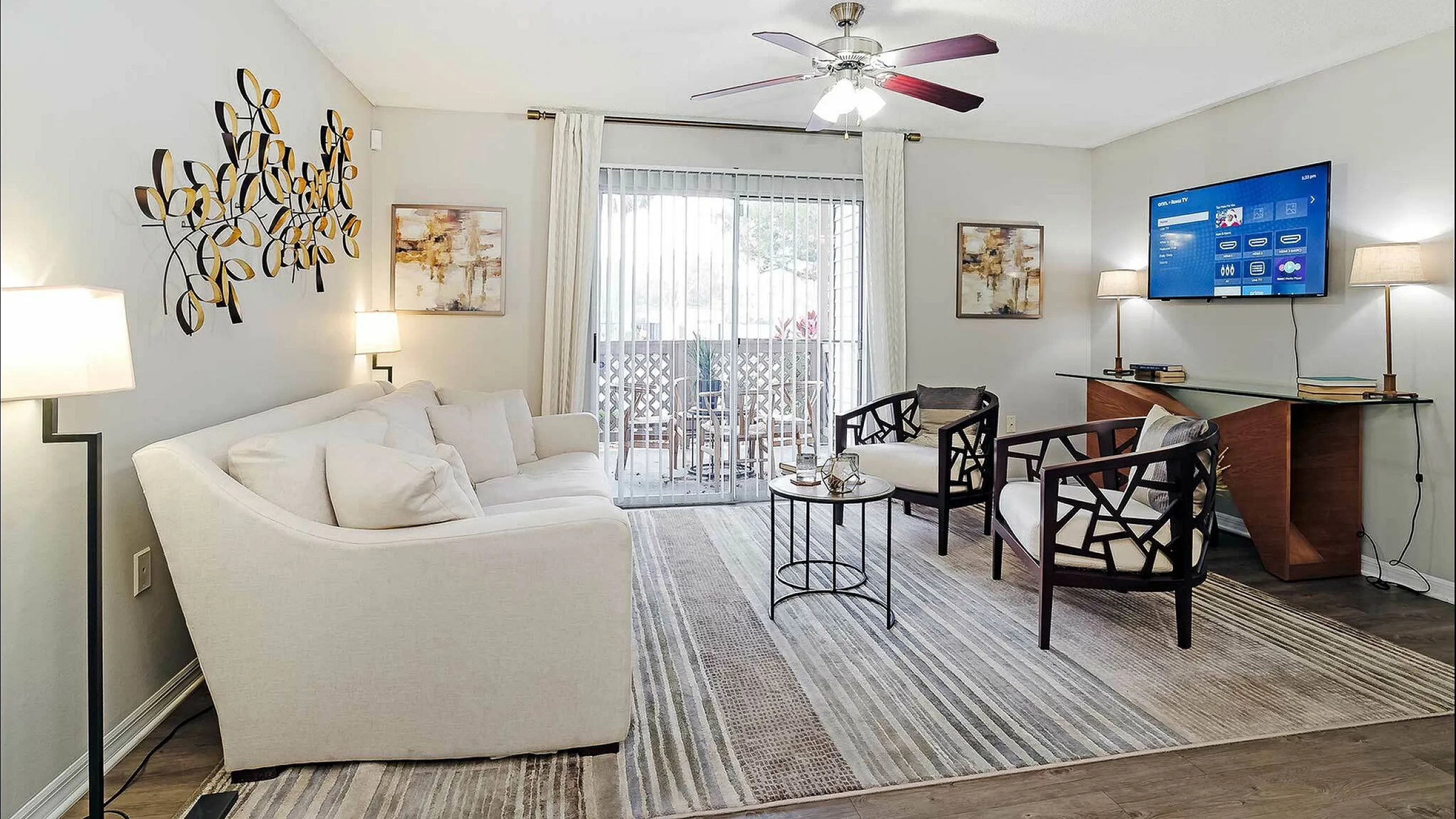Chic living room with cozy white sofa, modern wooden chairs, and elegant wall art, enhanced by natural light from sliding glass doors.