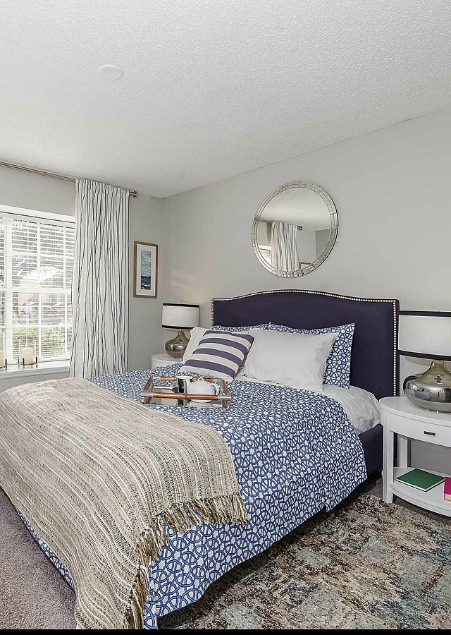 Bright and inviting bedroom with elegant decor, featuring a plush bed with patterned bedding, large window with striped curtains, and stylish bedside tables.