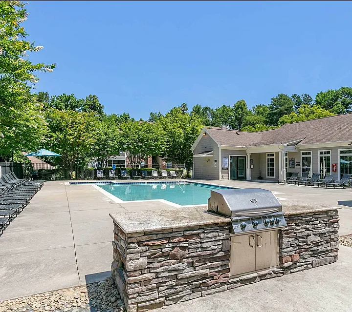 Inviting outdoor pool area with modern grilling station, sun loungers, and lush greenery, perfect for relaxation and entertaining.