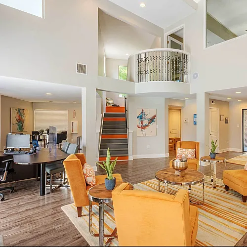Bright and inviting open-concept living room with high ceilings, featuring stylish orange armchairs, modern artwork, and sleek wooden flooring.