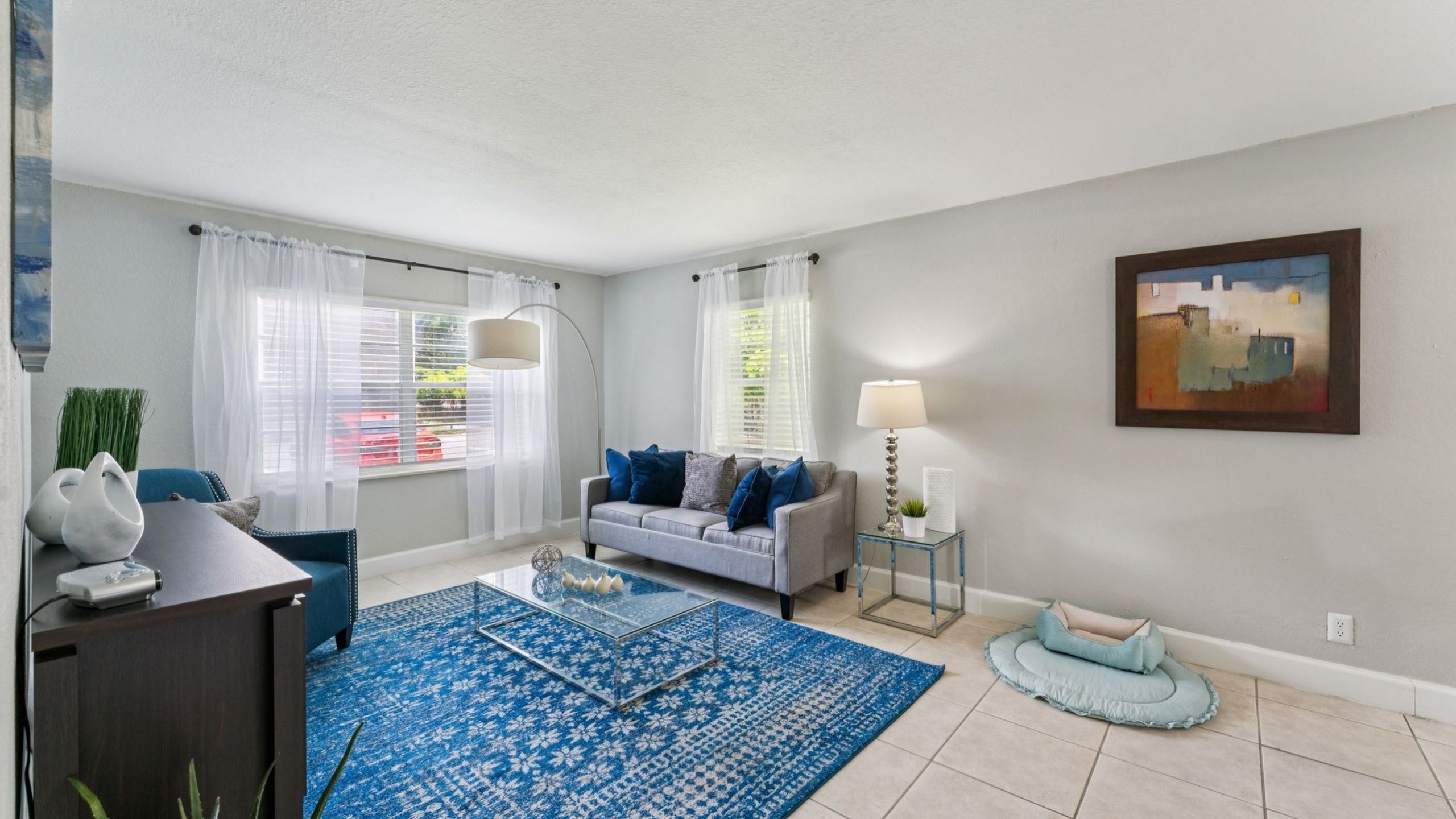 Elegant living room with a modern gray sofa, blue accents, and a designer glass coffee table on a stylish blue patterned rug.