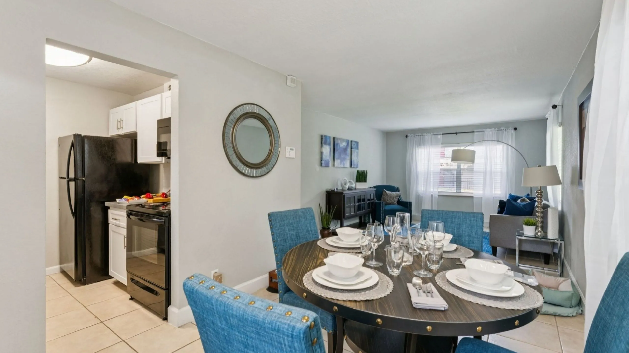 Elegant apartment interior showcasing a stylish dining area with blue textured chairs, a cozy living room, and a modern kitchen with sleek black appliances.