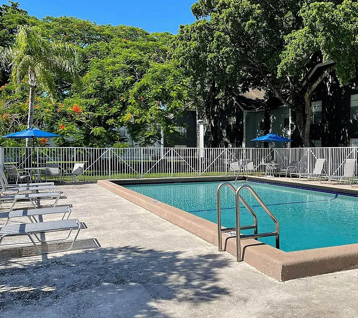 Inviting outdoor pool area with sun loungers, surrounded by lush greenery and vibrant flowers, perfect for relaxation.