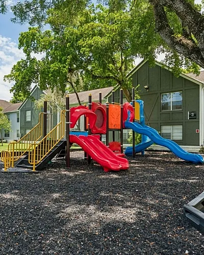Charming community playground with vibrant slides nestled under lush trees, set within a serene residential area.