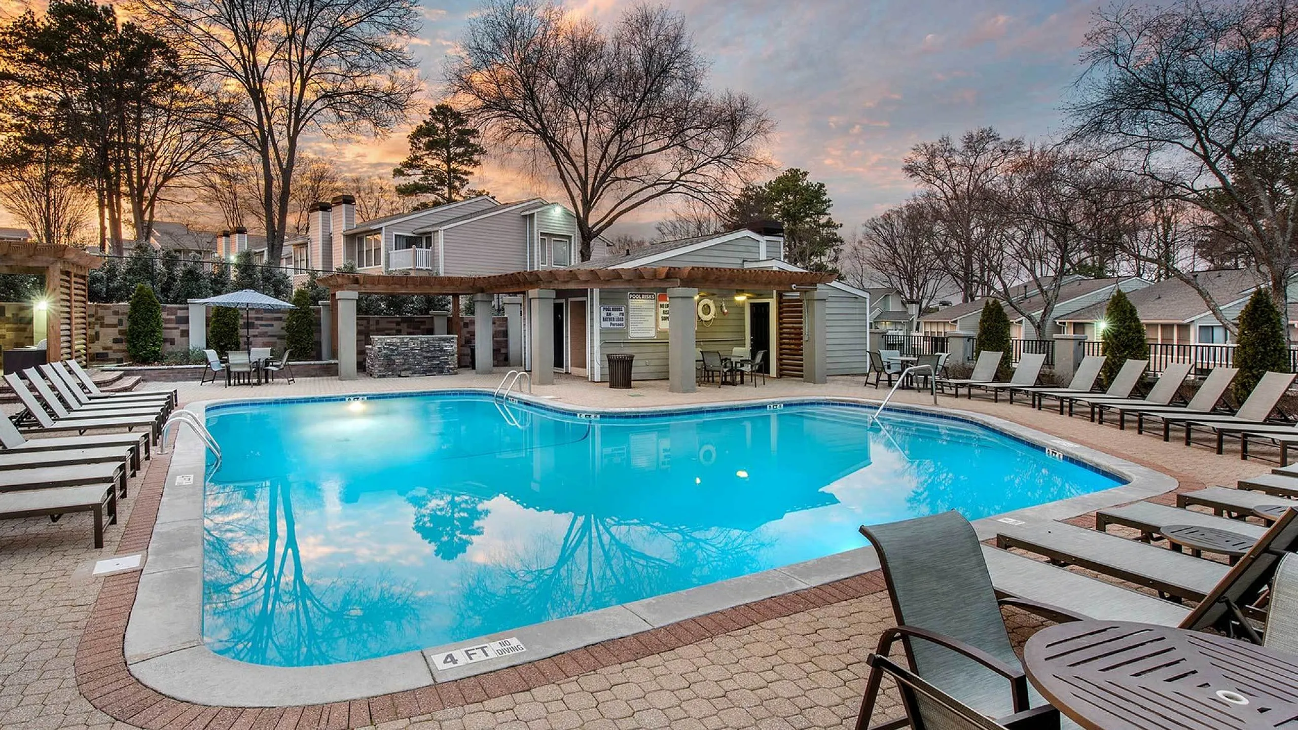 Inviting apartment complex with a luxurious outdoor pool surrounded by comfortable lounge chairs and a scenic sunset backdrop.