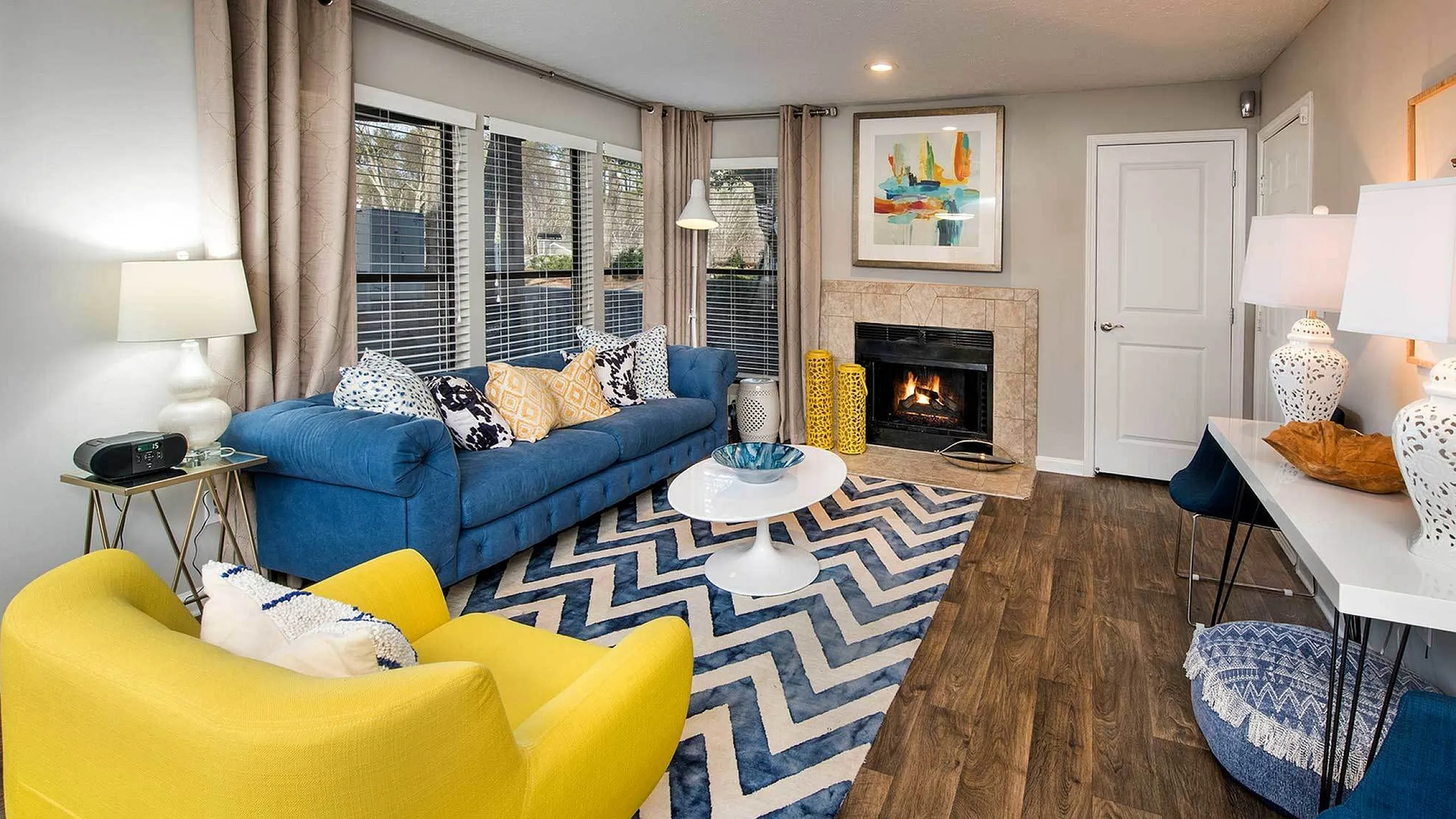 Chic living room with a cozy fireplace, vibrant blue and yellow seating, and stylish chevron rug, offering a modern and inviting ambiance.