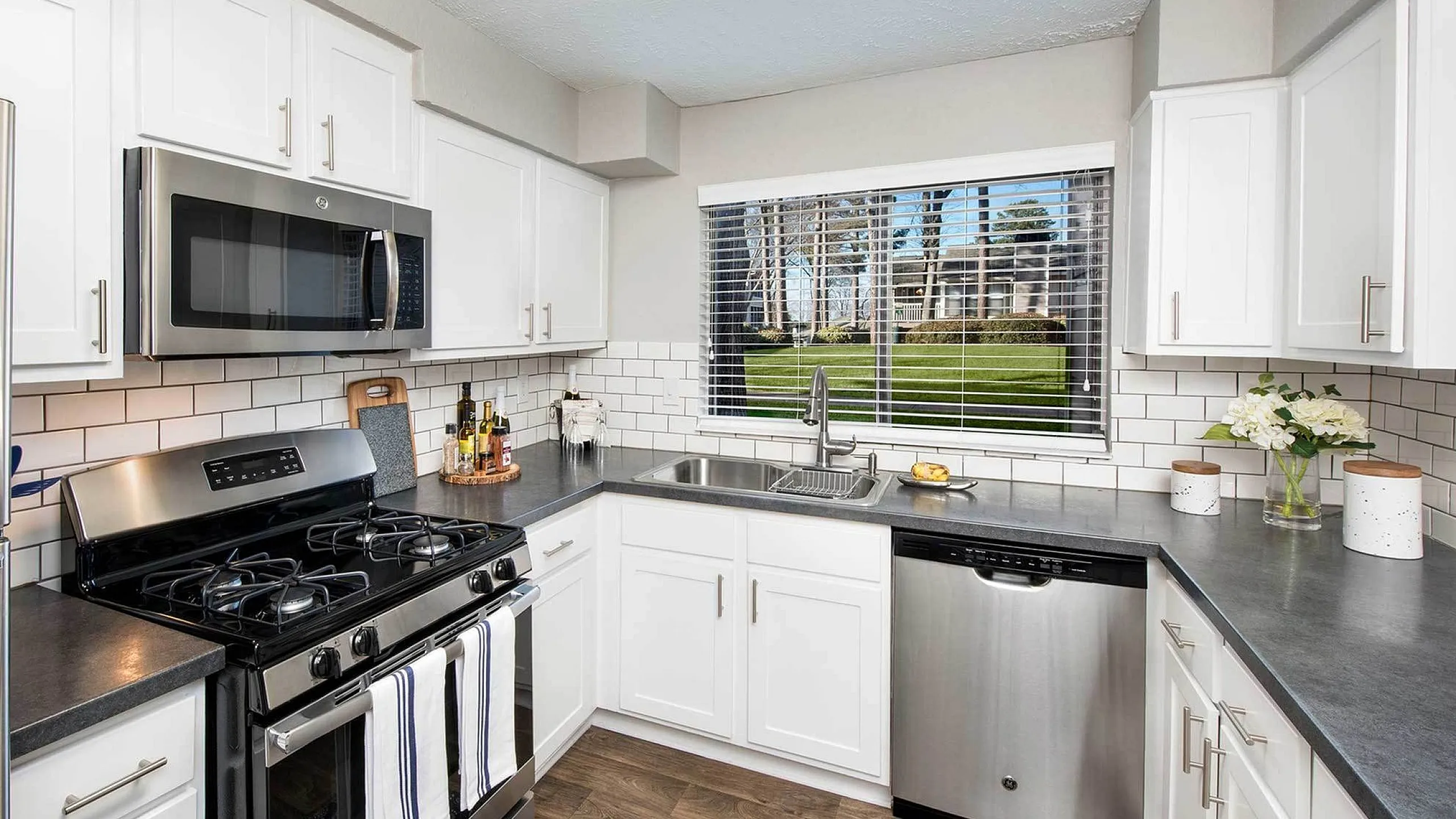 Modern kitchen with sleek stainless steel appliances, elegant white cabinetry, and a scenic view through a large window.