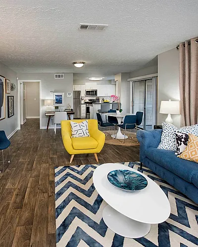 Modern open-concept living space with stylish decor, featuring a cozy blue sofa, vibrant yellow chair, and sleek kitchen area.