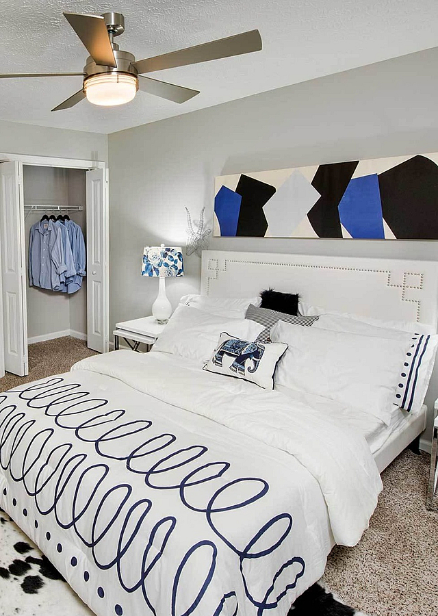 Chic bedroom with modern ceiling fan, abstract art, and stylish decor, exuding comfort and elegance.