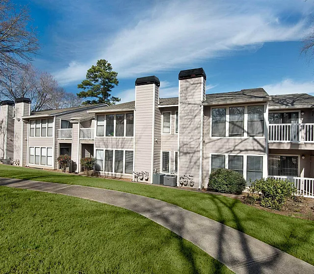 Charming apartment complex showcasing a modern facade with large windows, private balconies, and lush green surroundings, perfect for comfortable living.
