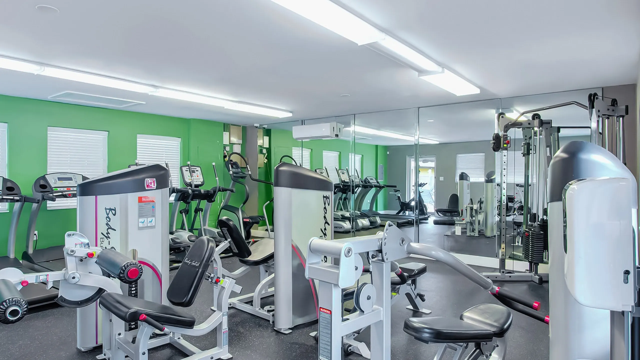 Modern fitness center with state-of-the-art exercise machines, vibrant green walls, and spacious mirrored interiors.