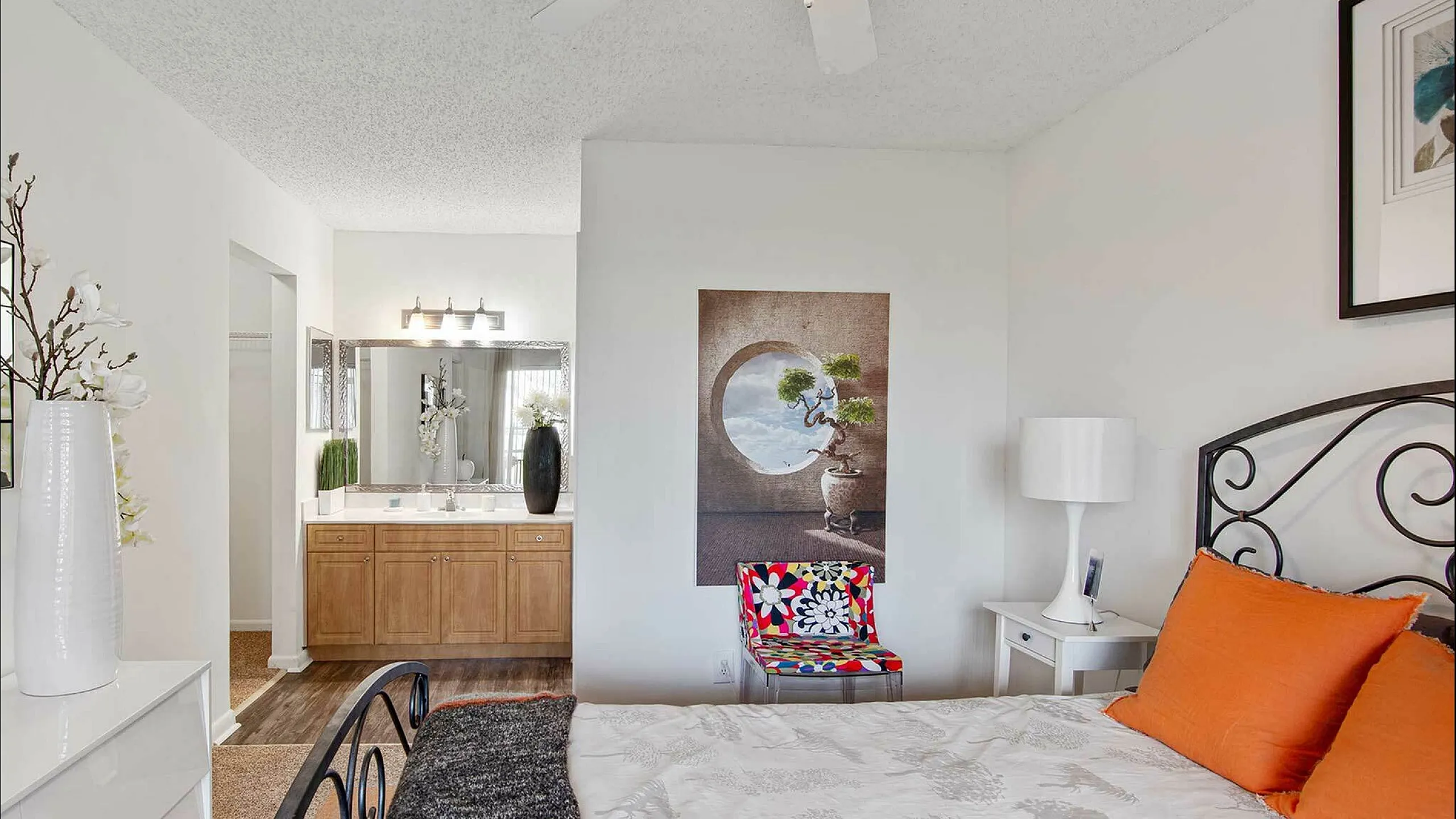 Bright and inviting bedroom with modern decor, featuring an elegant iron bed, vibrant cushions, and a well-lit vanity area.